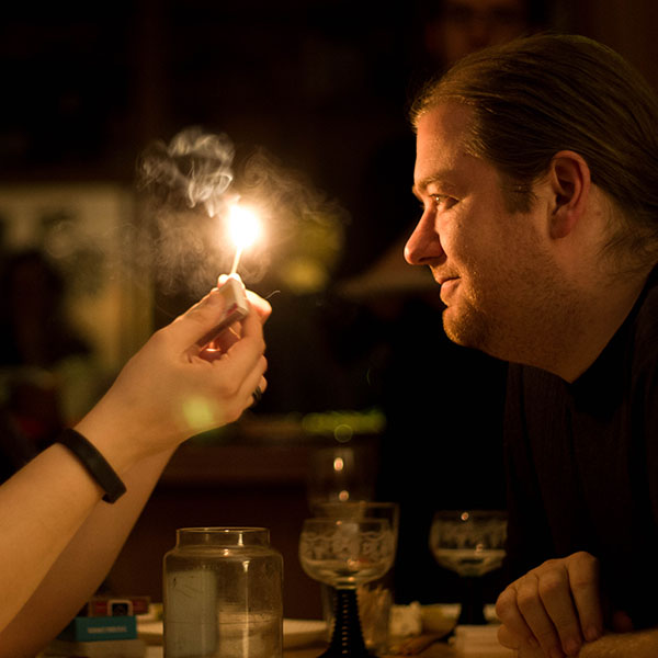 Two people stare at a smoking flame held between them